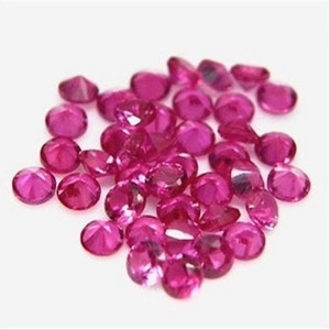 May include: A pile of loose pink ruby gemstones. The gemstones are round and have a shiny, polished finish.