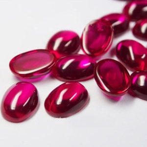 May include: A group of oval-shaped, bright red cabochon gemstones. The gemstones are smooth and polished, with a glossy finish.