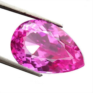 May include: A vibrant pink pear-shaped gemstone with a faceted cut. The gemstone is held in a pair of tweezers.
