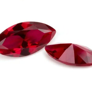 Può includere: Due pietre preziose rosse a forma di marquise, una più grande dell'altra, sono esposte su uno sfondo bianco.