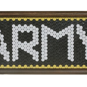 May include: A framed artwork featuring the word "ARMY" spelled out using white bullet casings on a black background. The frame is brown wood with a gold trim.