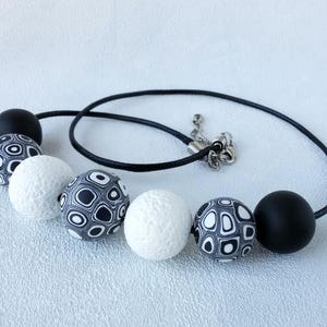 May include: A black and white patterned necklace with large round beads. The necklace has a black cord and a silver clasp.