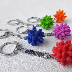 Pode incluir: Uma cole&ccedil;&atilde;o de chaveiros coloridos com designs esf&eacute;ricos e pontiagudos em vermelho, azul, verde, laranja e roxo. Cada chaveiro tem um anel e uma corrente de metal prateado.
