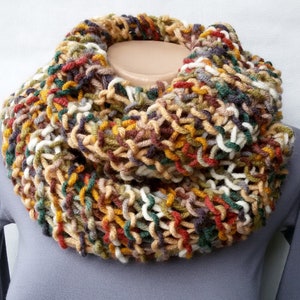 May include: A colorful knitted infinity scarf in shades of brown, green, white, red, and yellow. The scarf is made of a chunky yarn and has a loose, open weave.