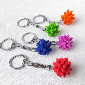 Pode incluir: Chaveiros com pingentes esf&eacute;ricos texturizados e coloridos em laranja, verde, roxo, azul e vermelho. Cada chaveiro tem um anel prateado e um acess&oacute;rio de elos de corrente. O fundo &eacute; uma superf&iacute;cie branca texturizada.