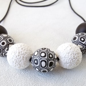 May include: A black and white necklace with large, round beads. The beads have different patterns, including a geometric pattern and a textured surface.