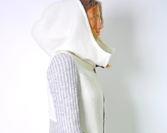 May include: A white hooded jacket with a gray knit panel and a white pocket. The jacket has a long, flowing design.