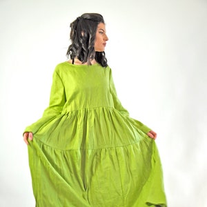 May include: A long, flowing green linen dress with a tiered skirt and long sleeves. The dress is loose-fitting and has a relaxed, casual style.