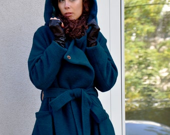 May include: A teal hooded coat with a wrap-around belt and large pockets. The coat has a button closure and is made of a textured fabric. The model is wearing black gloves and has a hood up.