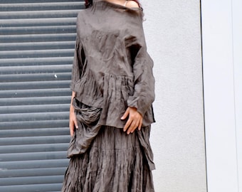 May include: A dark taupe two-piece outfit consisting of a long-sleeved top with an asymmetrical neckline and a matching floor-length skirt. The skirt features a gathered, tiered design with a textured, wrinkled fabric finish throughout the set.