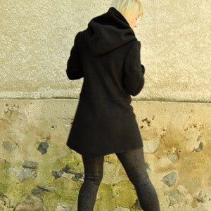 K&ouml;nnte beinhalten: Eine Frau in einem schwarzen Kapuzenmantel und schwarzen Leggings geht eine Steintreppe hinunter.