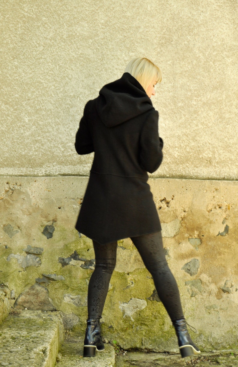 K&ouml;nnte beinhalten: Eine Frau in einem schwarzen Kapuzenmantel und schwarzen Leggings geht eine Steintreppe hinunter.