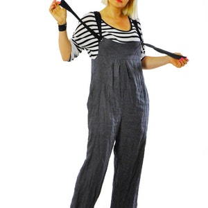 May include: A woman wearing a black and white striped shirt under a pair of dark gray overalls. The overalls have suspenders and are paired with black platform sandals. The woman is also wearing sunglasses.