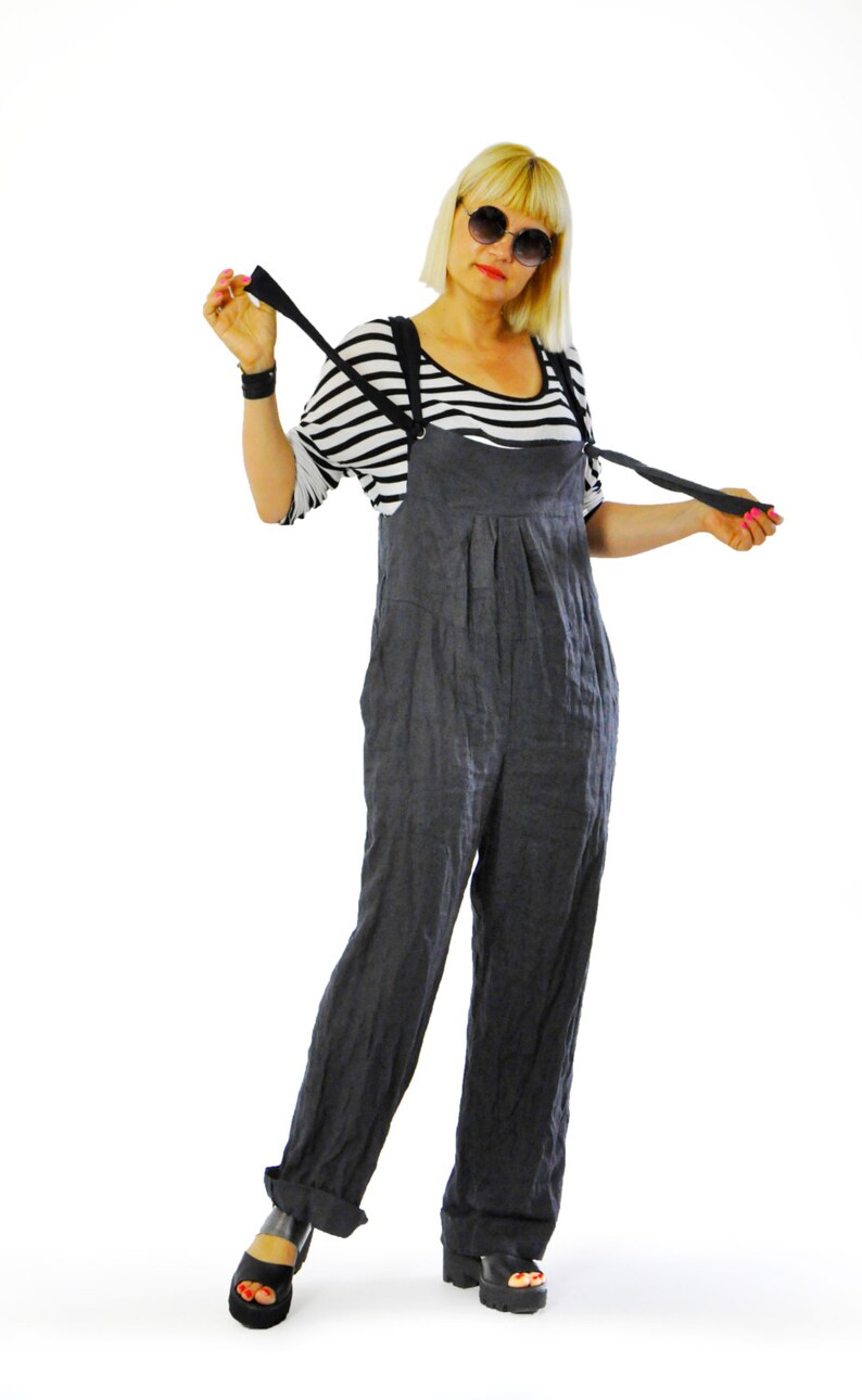 May include: A woman wearing a black and white striped shirt under a pair of dark gray overalls. The overalls have suspenders and are paired with black platform sandals. The woman is also wearing sunglasses.