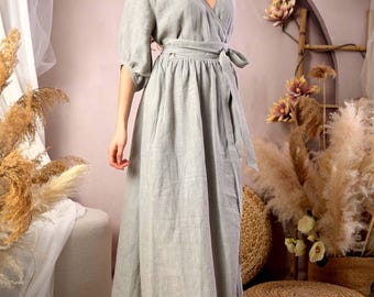 May include: A floor-length, light sage green wrap dress featuring a subtle checkered pattern, three-quarter length sleeves, and a matching fabric tie belt at the waist. The garment has a V-neckline and a full, flowing skirt that reaches the floor.