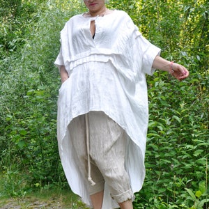 K&ouml;nnte beinhalten: Eine Frau tr&auml;gt ein wei&szlig;es Leinen-Tunika-Oberteil mit einem hohen, niedrigen Saum und eine beige Leinenhose. Sie tr&auml;gt gelbe Sandalen und eine Sonnenbrille.