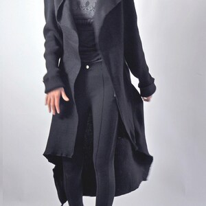 A slightly blurred action shot of a model in motion wearing a long black cardigan and white boots.