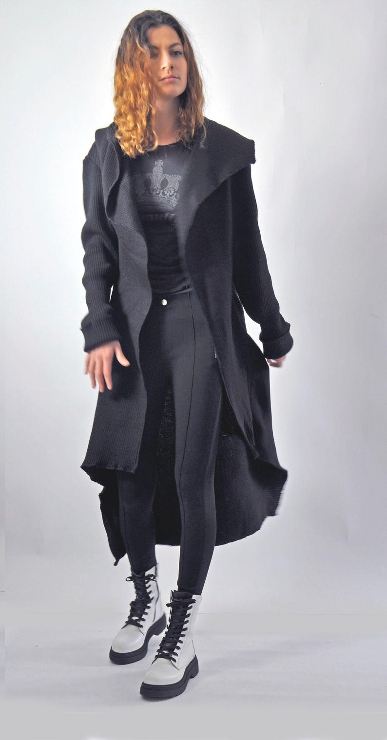 A slightly blurred action shot of a model in motion wearing a long black cardigan and white boots.