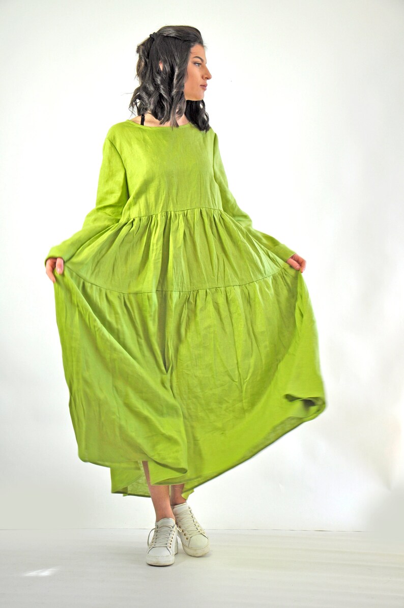 May include: A long, flowing green linen dress with a tiered skirt and long sleeves. The dress is loose-fitting and has a relaxed, casual style.