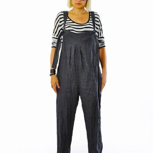 May include: A person wearing a dark gray linen jumpsuit with adjustable straps, paired with a black and white striped long-sleeve shirt. The outfit is completed with black platform sandals and sunglasses.