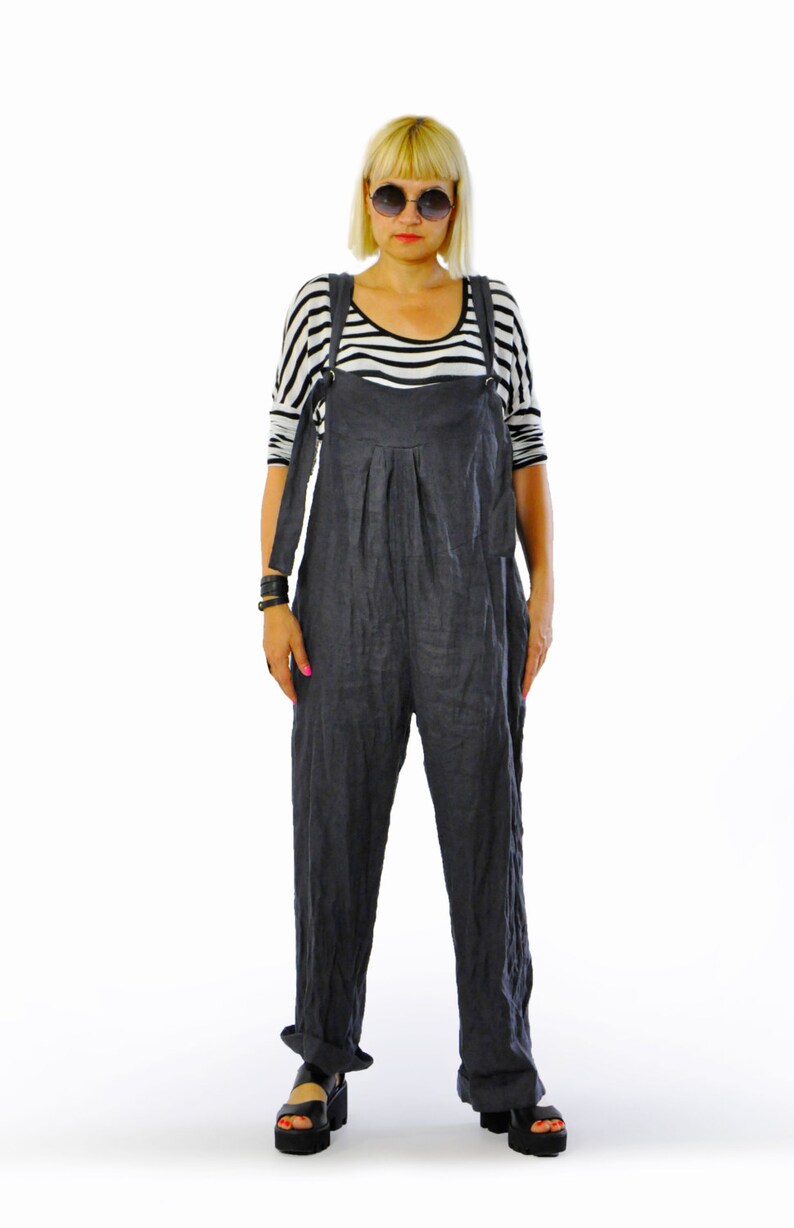 May include: A person wearing a dark gray linen jumpsuit with adjustable straps, paired with a black and white striped long-sleeve shirt. The outfit is completed with black platform sandals and sunglasses.