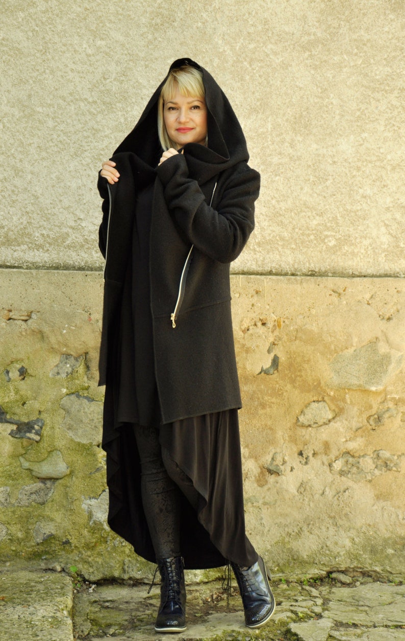 K&ouml;nnte beinhalten: Eine schwarze Kapuzenjacke mit einem langen, asymmetrischen Saum. Die Jacke hat einen Rei&szlig;verschluss und einen hohen Kragen.
