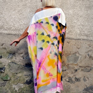 Puede incluir: Un vestido maxi blanco con un estampado abstracto en tonos de rosa, amarillo y azul. El vestido tiene una silueta suelta y fluida y un escote redondo.