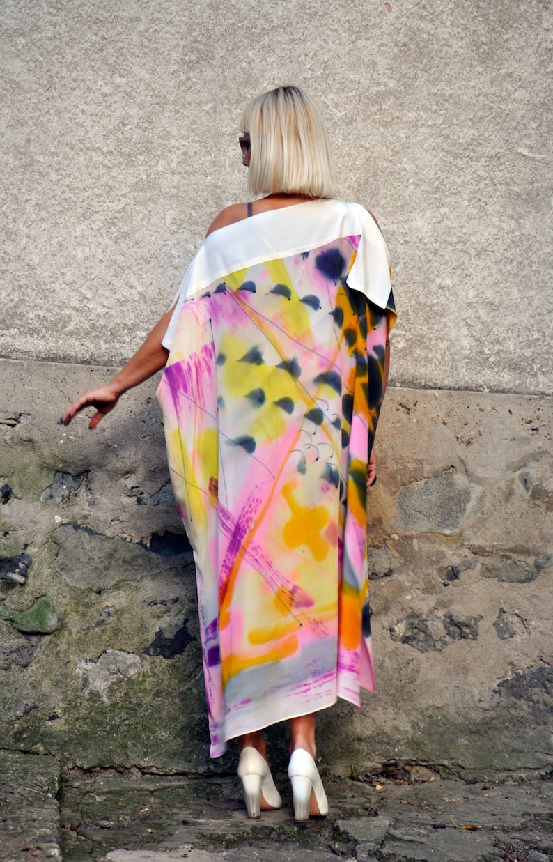 Puede incluir: Un vestido maxi blanco con un estampado abstracto en tonos de rosa, amarillo y azul. El vestido tiene una silueta suelta y fluida y un escote redondo.