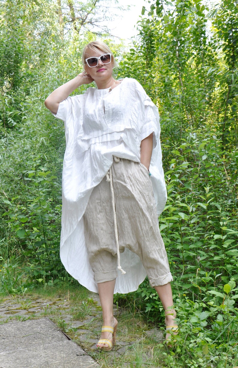 K&ouml;nnte beinhalten: Eine Frau tr&auml;gt ein wei&szlig;es Leinenoberteil mit R&uuml;schenkragen und eine beige Leinenhose mit Kordelzug. Sie tr&auml;gt eine wei&szlig;e Sonnenbrille und gelbe Sandalen.