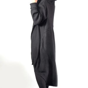 A side profile view of a woman with her hood up, modeling a long black ribbed knit cardigan.