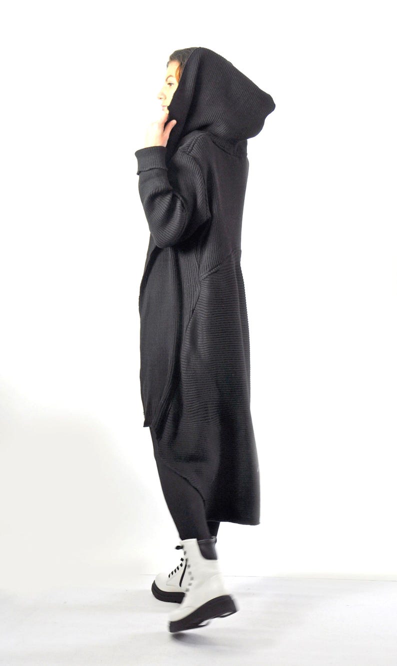 A side profile view of a woman with her hood up, modeling a long black ribbed knit cardigan.