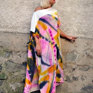 Puede incluir: Una mujer lleva un vestido maxi de estampado abstracto blanco y rosa con un top blanco. El vestido tiene una abertura lateral y est&aacute; hecho de una tela fluida. Lleva gafas de sol blancas y tacones blancos.