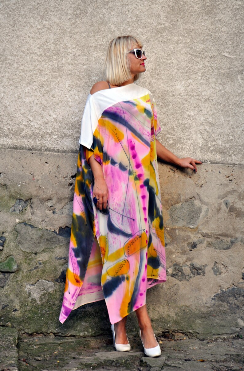 Puede incluir: Una mujer lleva un vestido maxi de estampado abstracto blanco y rosa con un top blanco. El vestido tiene una abertura lateral y est&aacute; hecho de una tela fluida. Lleva gafas de sol blancas y tacones blancos.