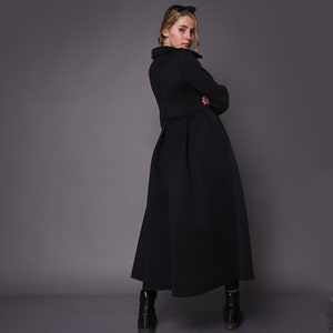 May include: A black long-sleeved dress with a high collar and a flared skirt. The dress is made of a thick, textured fabric. The model is wearing black boots.