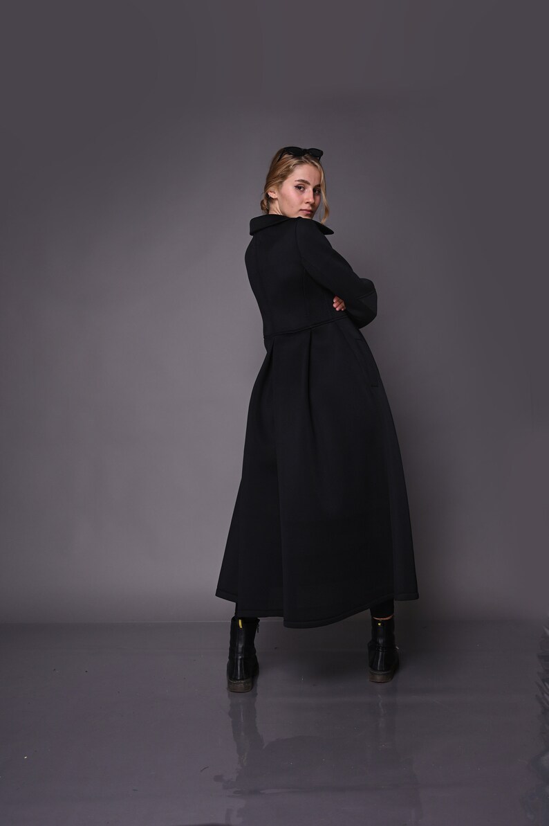 May include: A black long-sleeved dress with a high collar and a flared skirt. The dress is made of a thick, textured fabric. The model is wearing black boots.