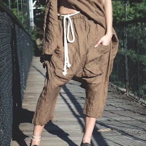 Può includere: Completo in lino marrone composto da un top a maniche corte e pantaloni larghi con coulisse bianca. I pantaloni hanno tasche. La persona indossa sandali e si trova su un ponte di legno.