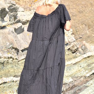 May include: A black tiered maxi dress with a slightly off-the-shoulder neckline. The dress is made of a soft, flowy fabric and has a relaxed fit. The model is wearing the dress with black sandals.