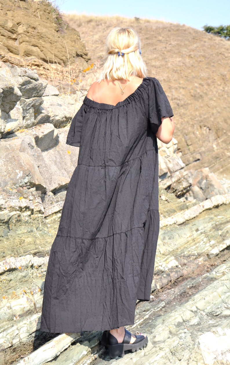 May include: A black tiered maxi dress with a slightly off-the-shoulder neckline. The dress is made of a soft, flowy fabric and has a relaxed fit. The model is wearing the dress with black sandals.