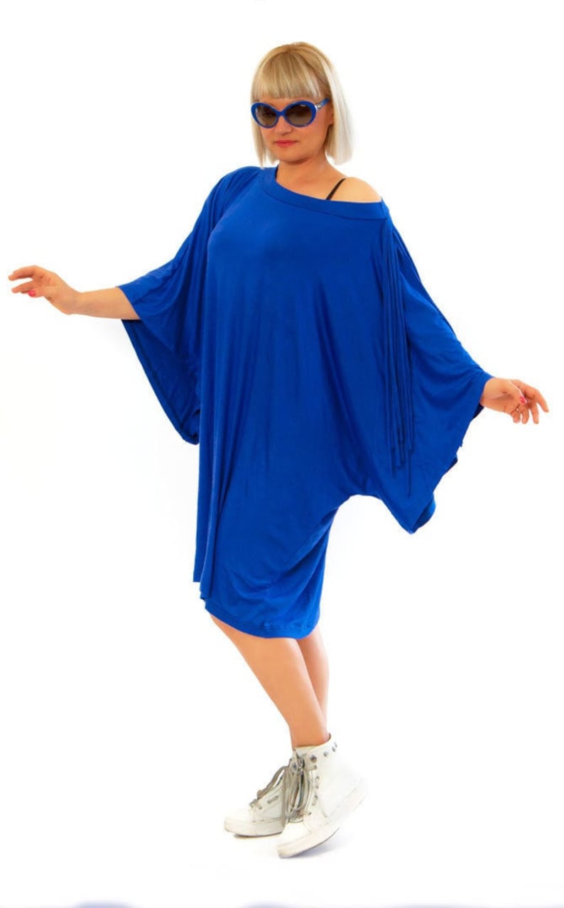 May include: A vibrant blue, loose-fitting dress with wide sleeves. The dress is knee-length and paired with white high-top sneakers. The model is wearing sunglasses. The overall style is casual and comfortable.