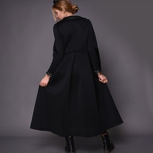 May include: A black long-sleeved coat with a high collar and a pleated skirt. The coat has gold trim on the cuffs and a belt.
