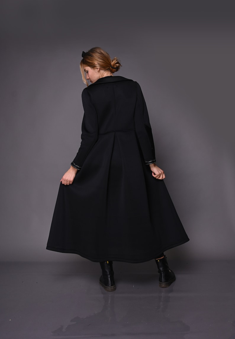 May include: A black long-sleeved coat with a high collar and a pleated skirt. The coat has gold trim on the cuffs and a belt.