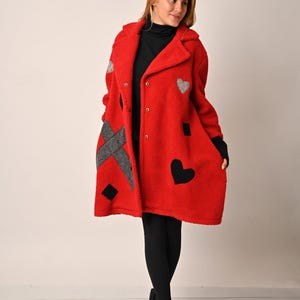 May include: A red fleece coat with black and grey geometric patches and heart designs. The coat has a button closure and a collar.