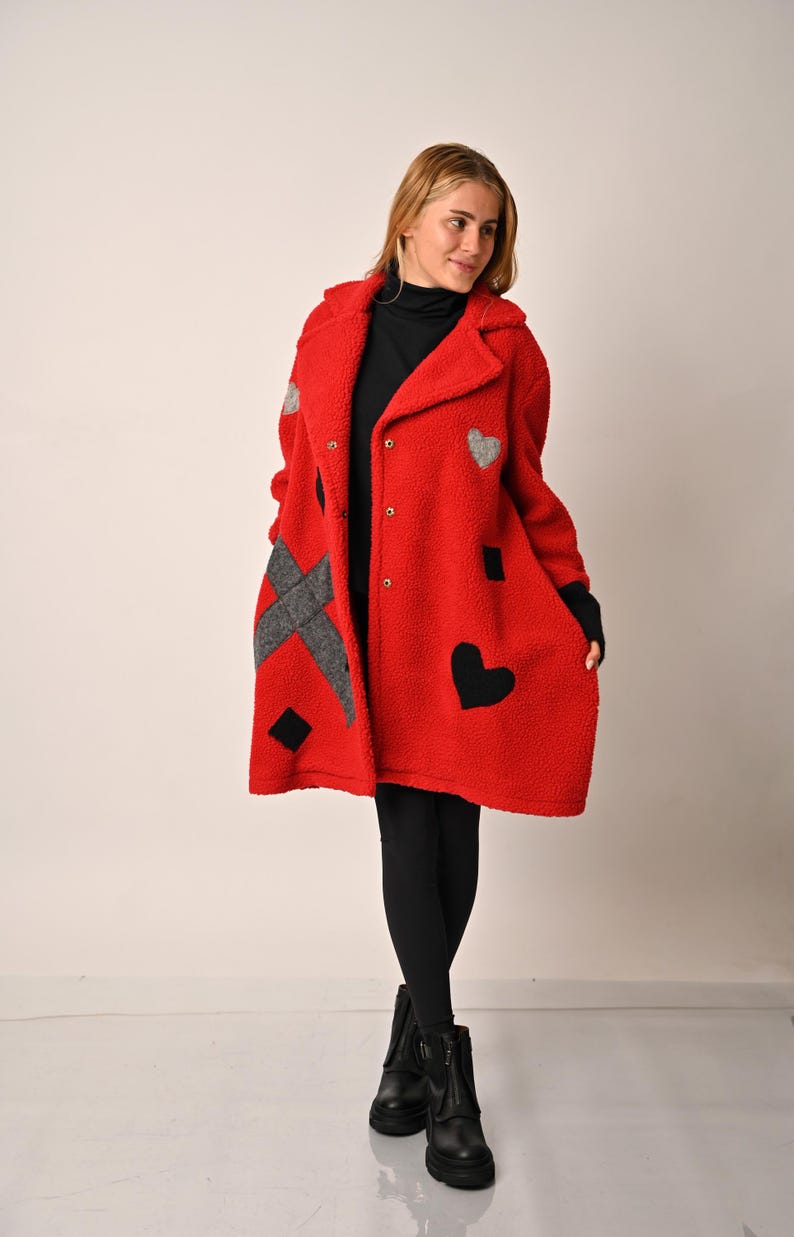 May include: A red fleece coat with black and grey geometric patches and heart designs. The coat has a button closure and a collar.