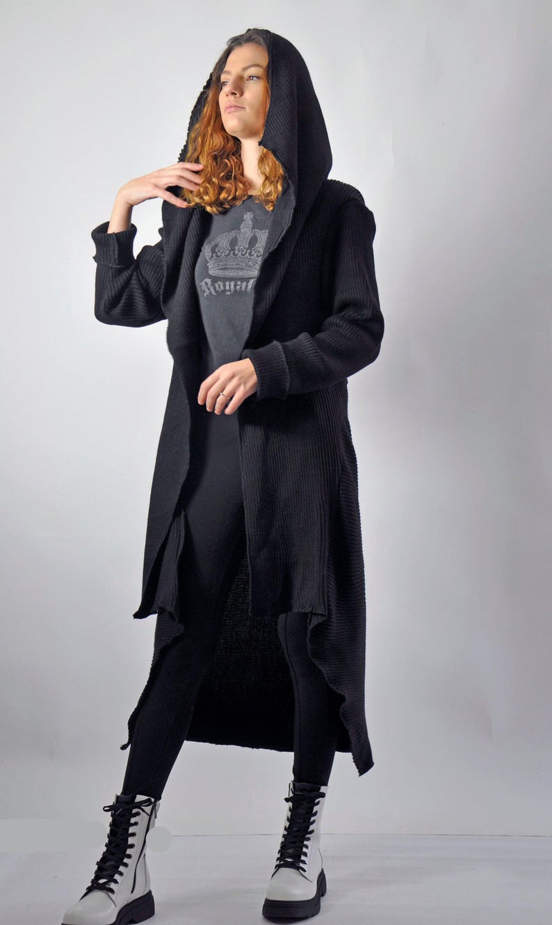 A full-length front view of a woman wearing a black maxi cardigan with a hood, layered over a grey shirt and black leggings.