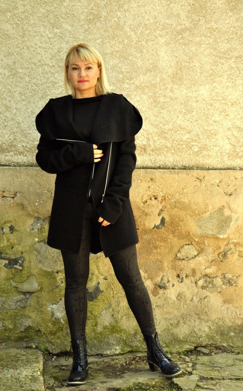 K&ouml;nnte beinhalten: Eine Frau tr&auml;gt einen schwarzen Langarmmantel mit gro&szlig;em Kragen und Rei&szlig;verschluss. Sie tr&auml;gt eine schwarze Leggings und schwarze Stiefel.