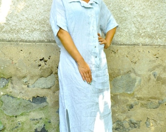 May include: A light blue, floor-length linen dress featuring short sleeves, a collared neckline, a front button-down closure, and a high side slit. The garment is paired with black platform sandals and dark-tinted sunglasses with a patterned frame.