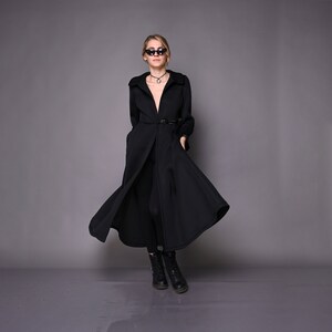 May include: A black long-sleeved coat with a deep V-neckline and a belt. The coat has a flowing skirt and is worn with black leggings and black boots.
