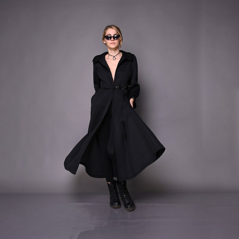 May include: A black long-sleeved coat with a deep V-neckline and a belt. The coat has a flowing skirt and is worn with black leggings and black boots.