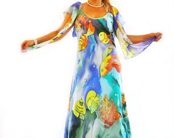 May include: A floor-length sleeveless dress featuring a vibrant underwater scene with colorful fish, coral, and seaweed patterns in shades of blue, yellow, and orange. The garment has a V-neckline and flowing, sheer cape-like sleeves. The text gabyga is visible.