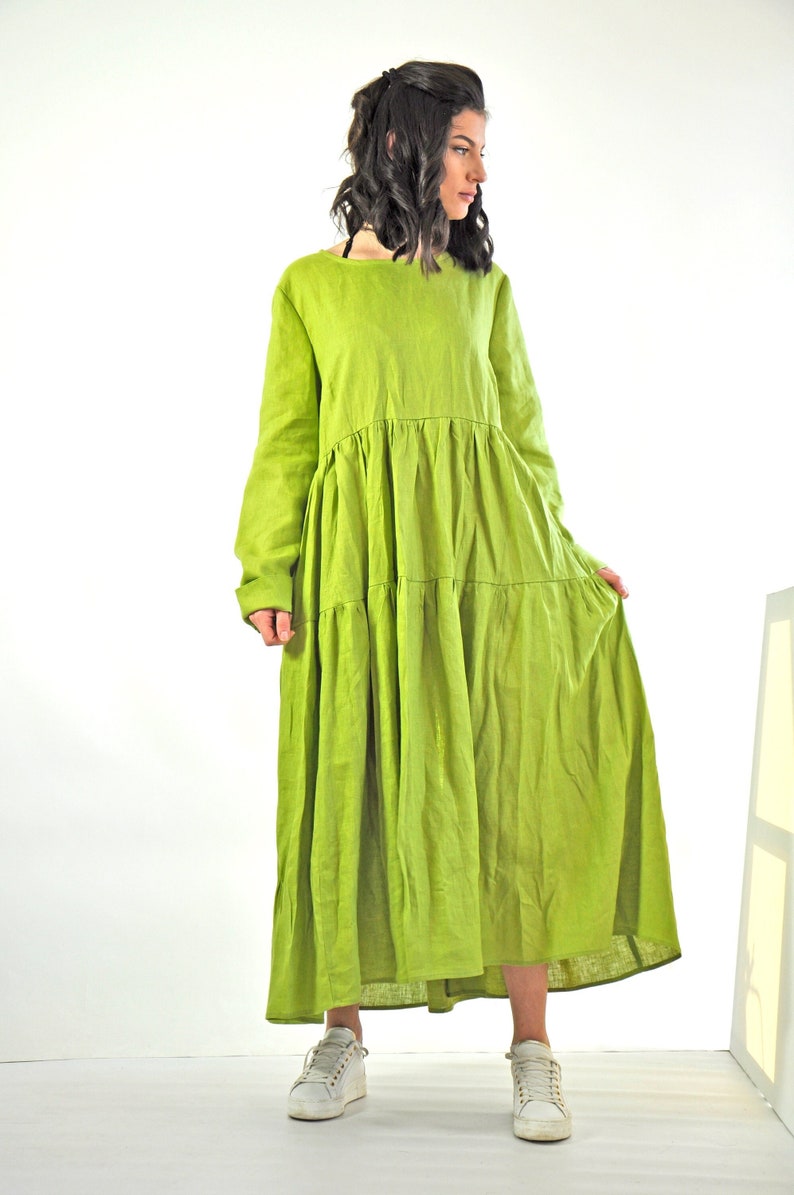 May include: A long, tiered, green linen dress with long sleeves. The dress is loose-fitting and has a relaxed silhouette.